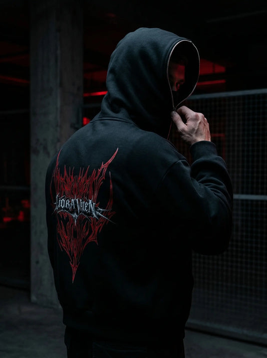 Person wearing a black hoodie with a red and white logo on the back, standing in a dark setting.