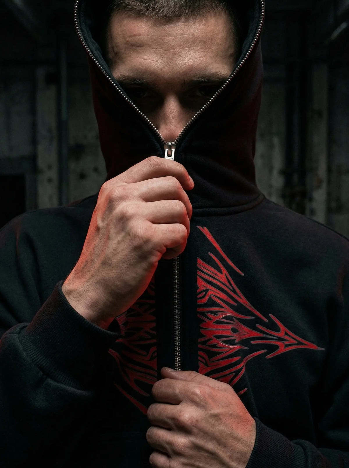Person wearing a black hoodie with a red tribal design, holding the zipper.